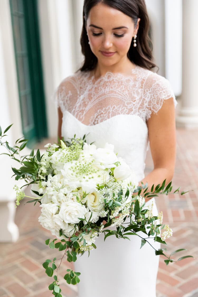 Women wearing a white wedding dress holding a luxury floral bouquet with white flowers and greenery.
