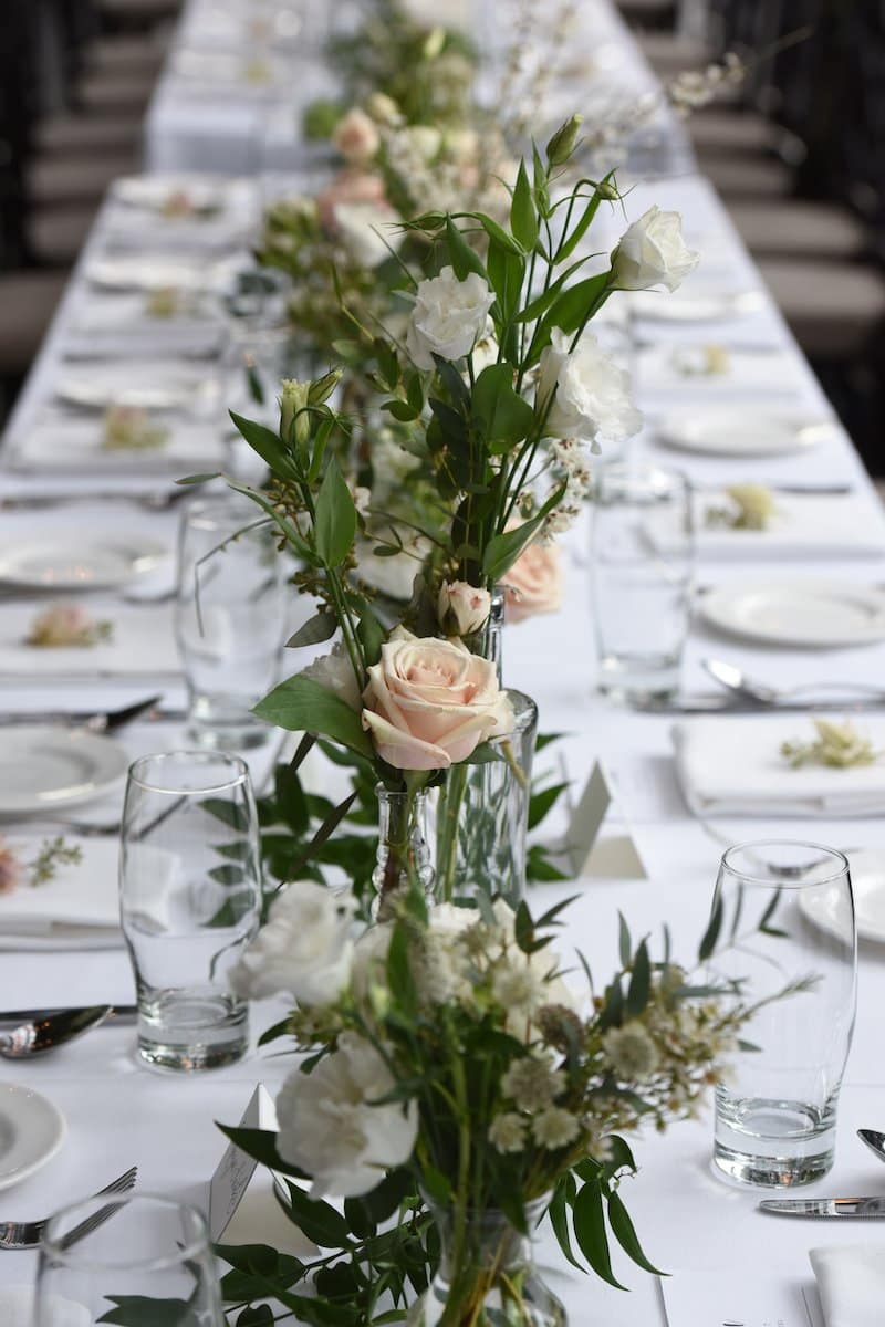 Long white dining table set for an event with delicate white floral arrangements.