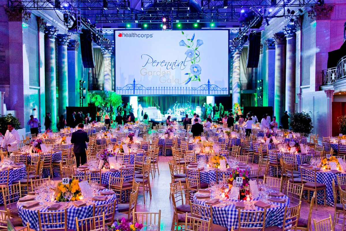 Gala dinner setup with blue gingham tablecloths and center stage screen reading "Perennial Garden Gala"
