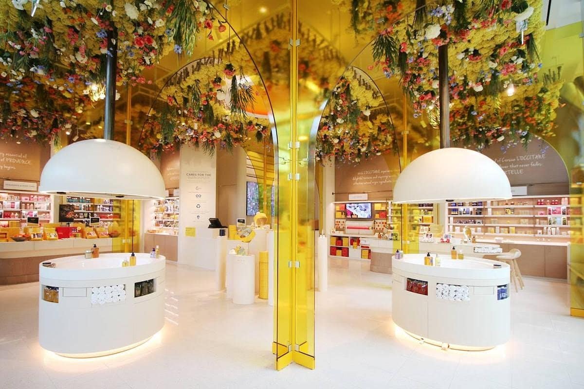 Interior of L'Occitane store with white counters and a ceiling covered in colorful flowers.