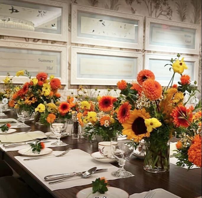 A rustic table setting with a bright floral centerpiece featuring sunflowers and orange flowers.