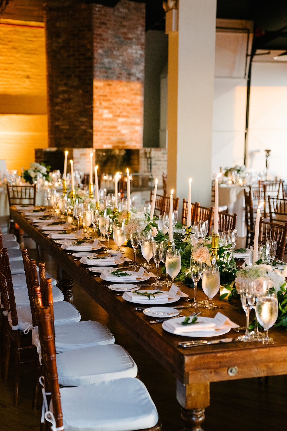 Rustic dinner tablescape on a wooden table with white and green flowers along the center with candlesticks throughout.