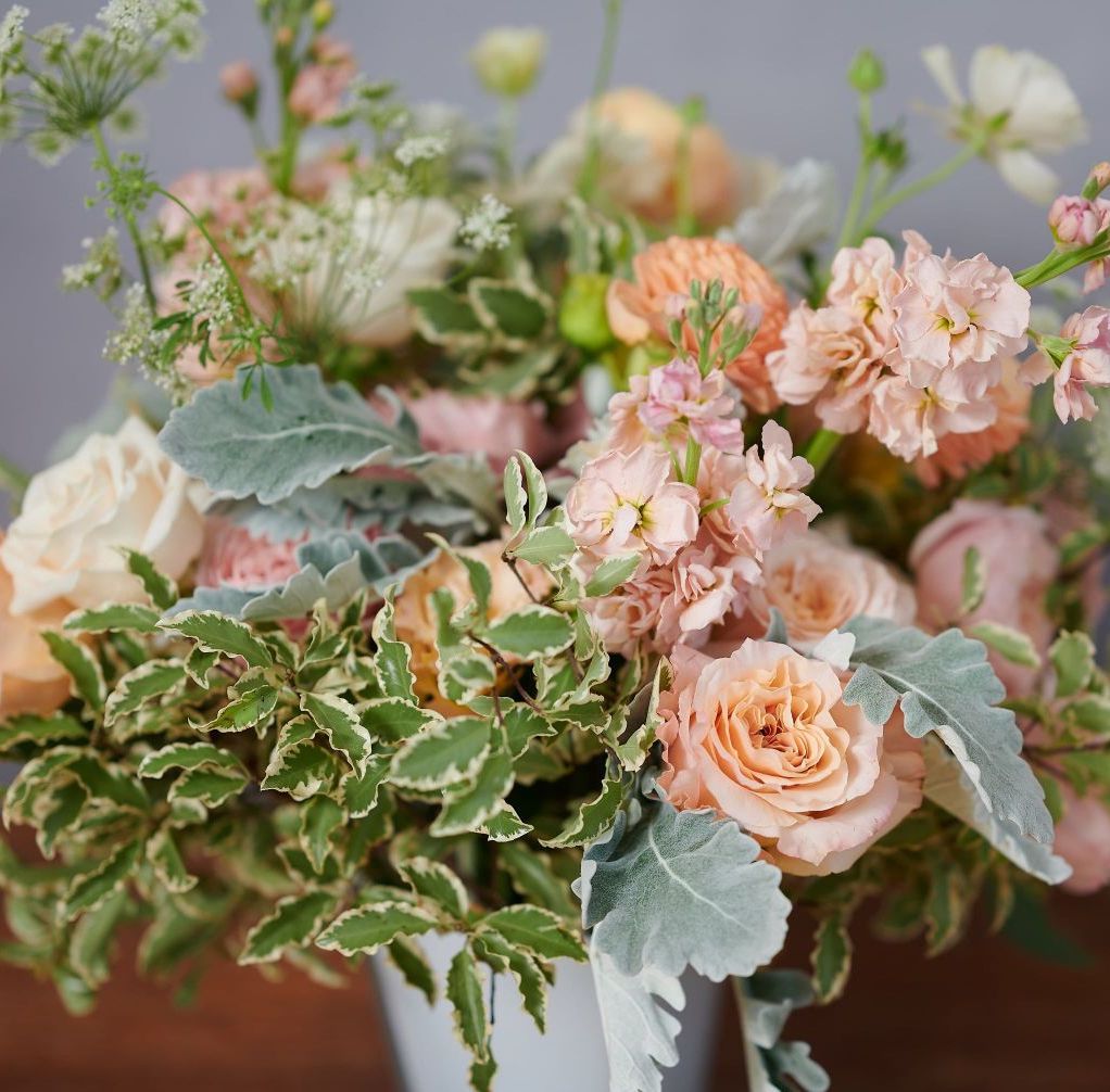 Orange and pink hued floral arrangement with greenery on a gray background