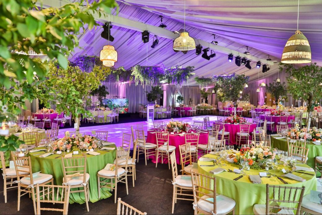 A gala tent with purple lighting and tables set with lime green and fuchsia linens and floral centerpieces