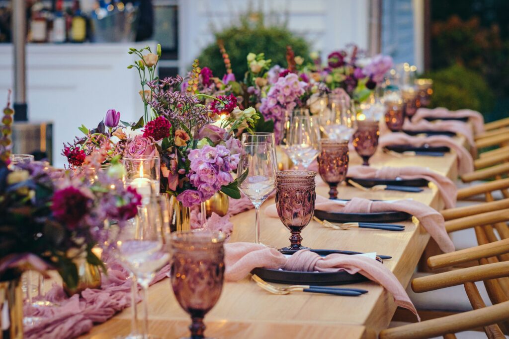 Long wooden tables at an event with pink table runners, flowers, and lit candles in glass holders
